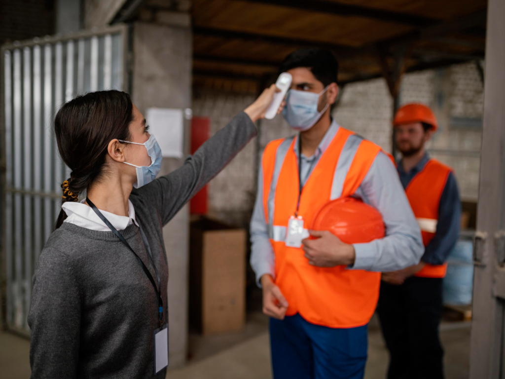 Mujer tomando una prueba de temperatura a un hombre con chaleco de seguridad anaranjado